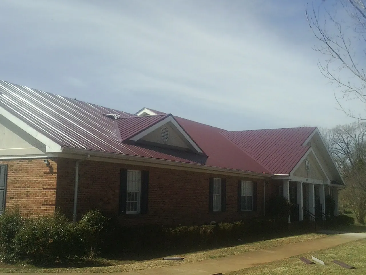 Red metal roof with gabled entries on a long brick building, from a Hail Damage Roof Repair job in Babson Park