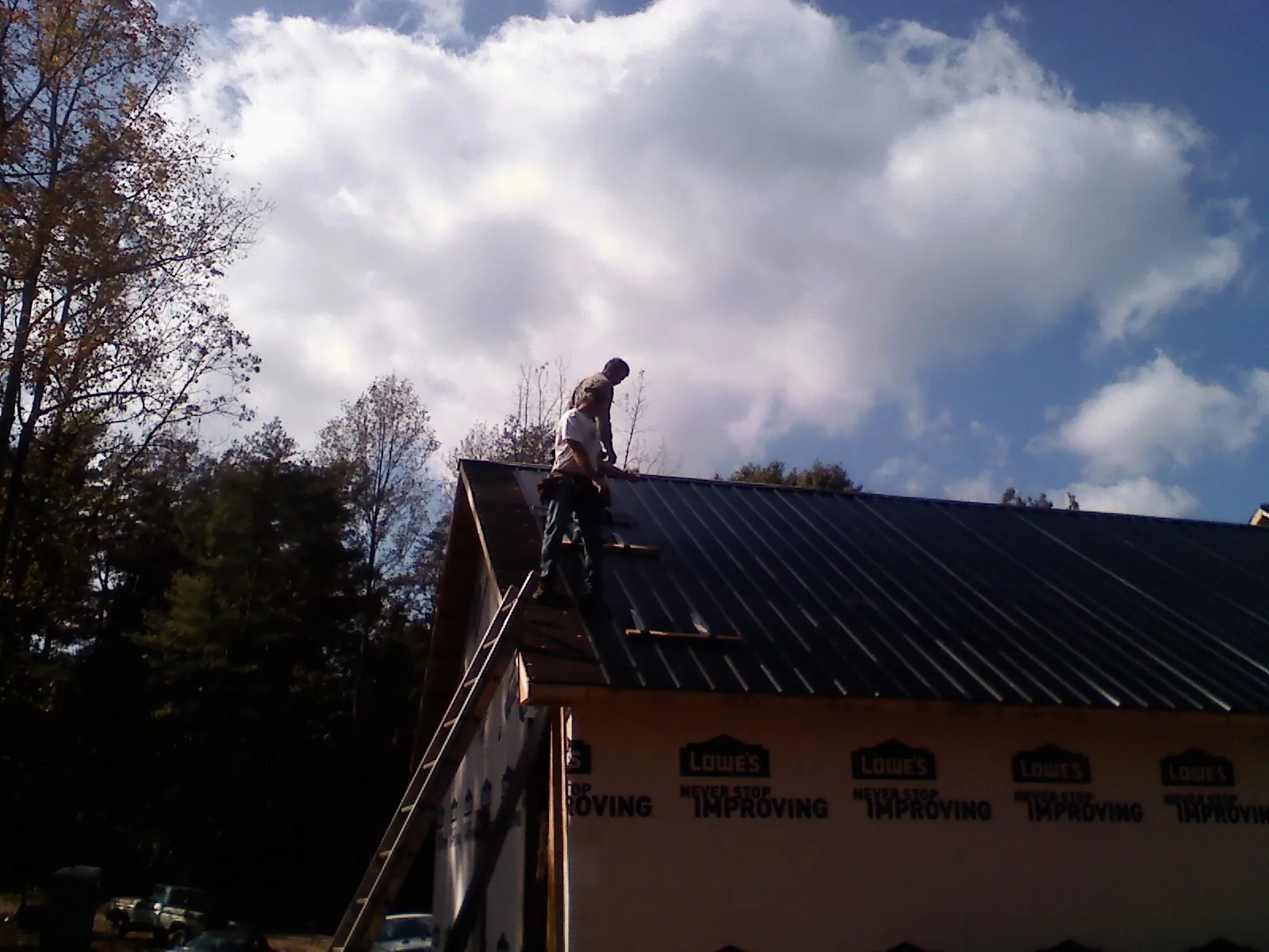 Roofer fastening dark metal panels high against a cloudy sky, from a Roof Inspection job in Babson Park