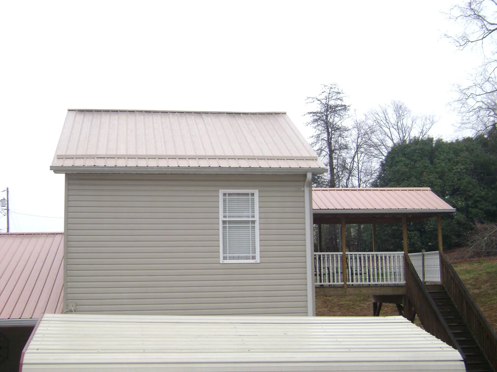 Tan metal roofs on a two story addition and attached porch, from a Roof Replacement job in Babson Park